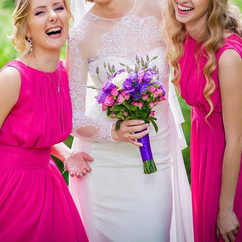 Two women wearing custom long chiffon bridesmaid dress in bright pink standing beside bride in white dress holding purple bouquet