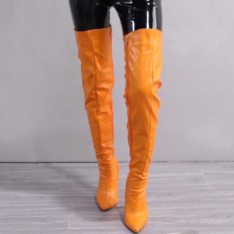Bright orange pointed toe long boots for women worn with black shiny pants on gray floor
