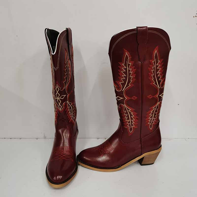Vintage knee high cowboy boots in dark red leather with decorative stitching and wooden heels