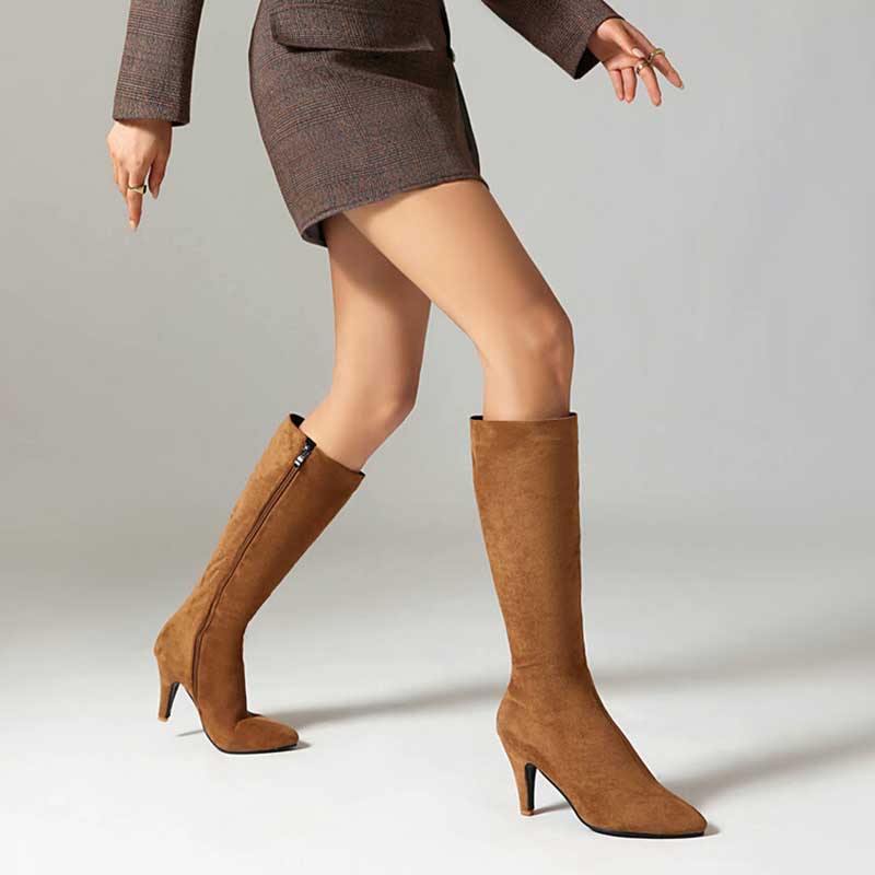 Brown women's suede knee-high boots with side zipper and pointed toe worn with a brown skirt suit