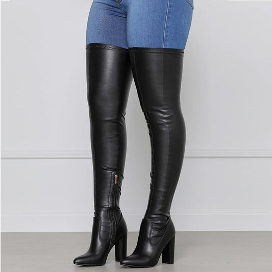 Black chunky heeled over the knee boots worn with blue jeans on a white background