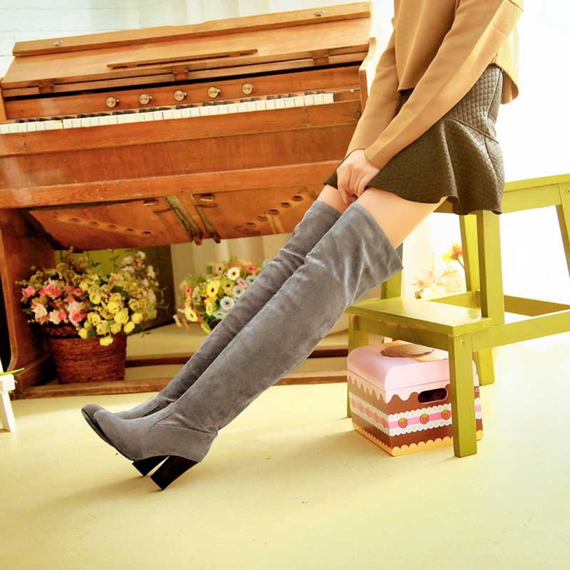 Gray suede plus size thigh high boots for women worn with a short skirt seated on a green chair
