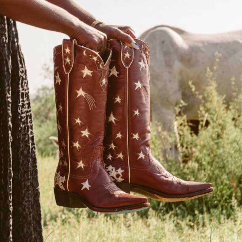 Brown leather star pattern knee high boots held outdoors with a horse in the background