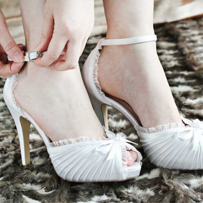 Elegant white bow bridal heels with ankle strap and pleated design worn on feet