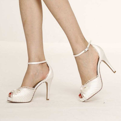 White bow bridal heels with ankle strap and high stiletto heel worn on feet